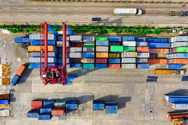 aerial view of shipping containers being moved next to a road with a passing truck