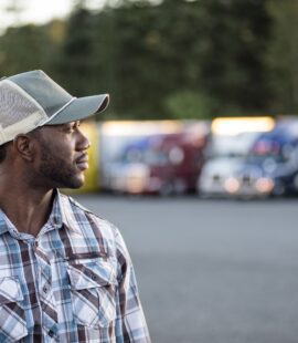 Black man truck driver near his truck parked in a parking lot at a truck stop